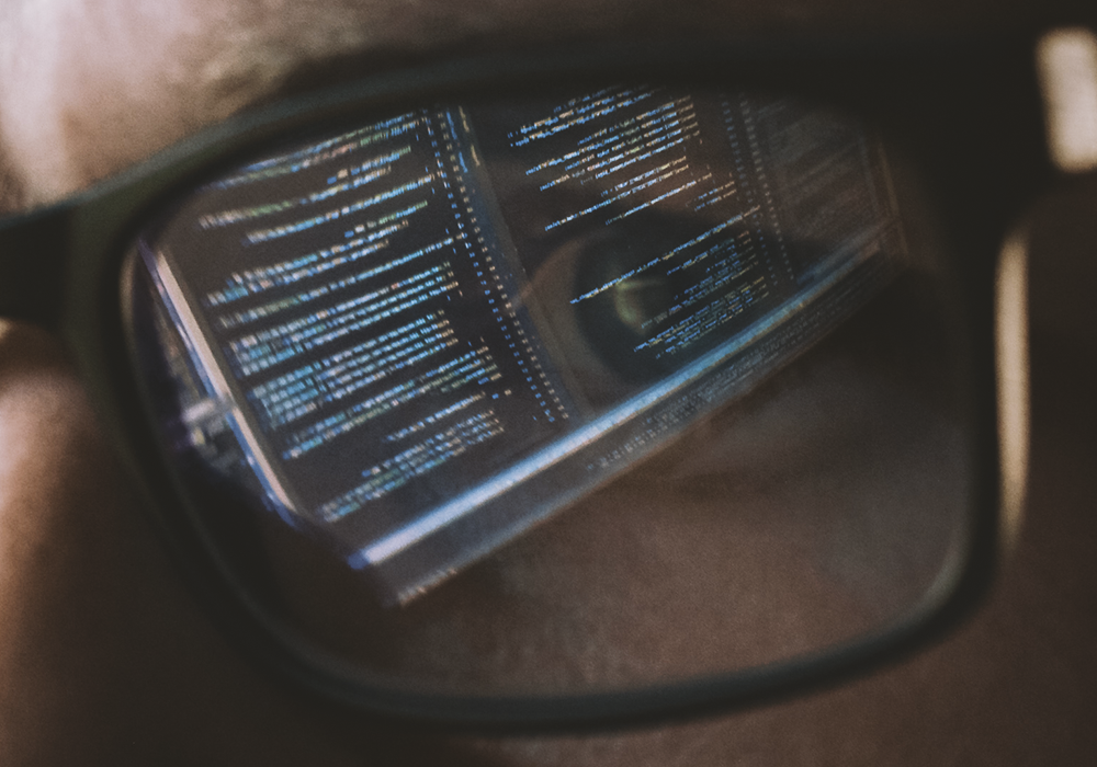 A page of code on a computer screen reflected in a pair of eyeglasses worn by a programmer.