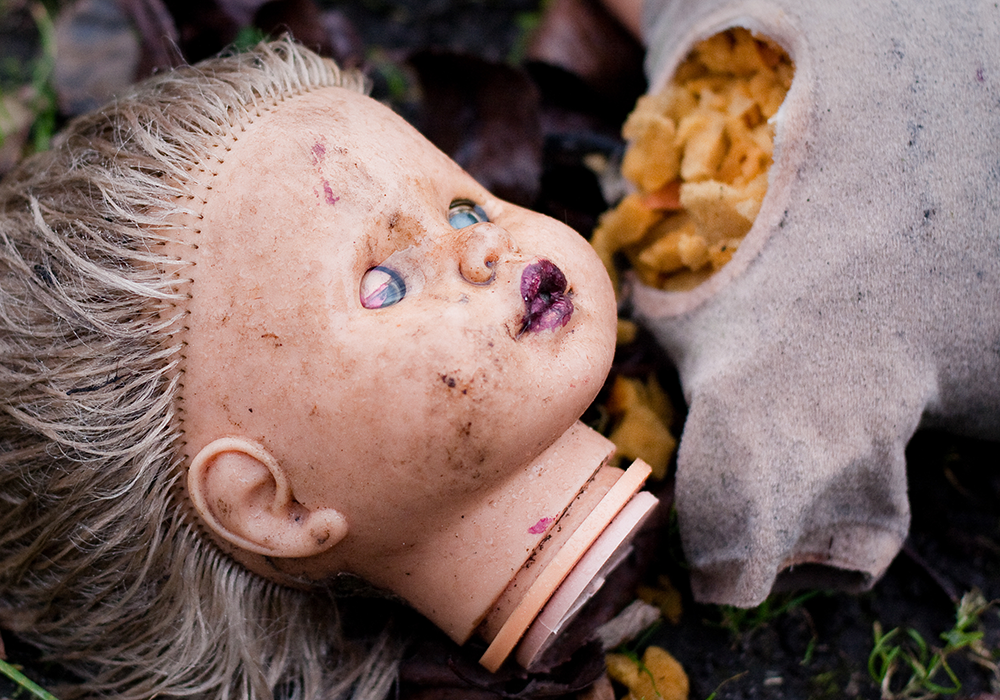 Une tête de poupée détachée du corps gît sur l’herbe.